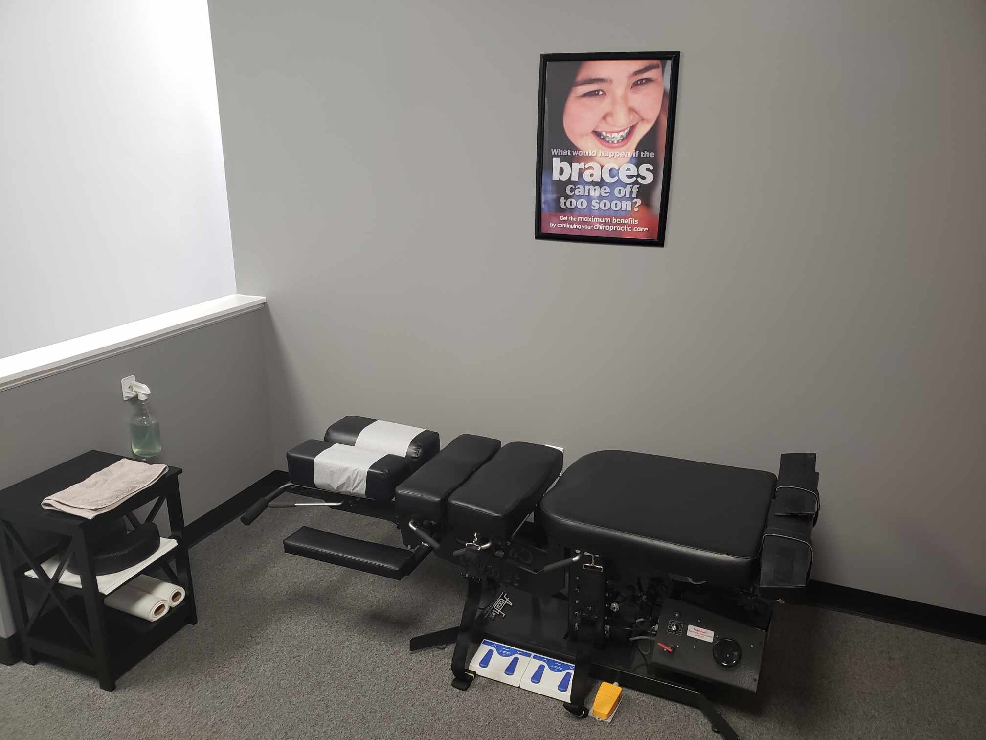 Adjusting room with a black chiropractic table, side table with towels and a framed poster