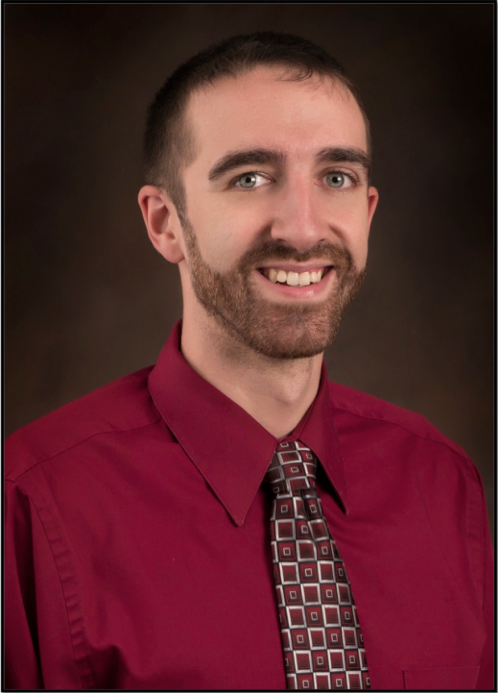 Portrait of Dr. Kevin McDade smiling, in a red shirt and patterned tie