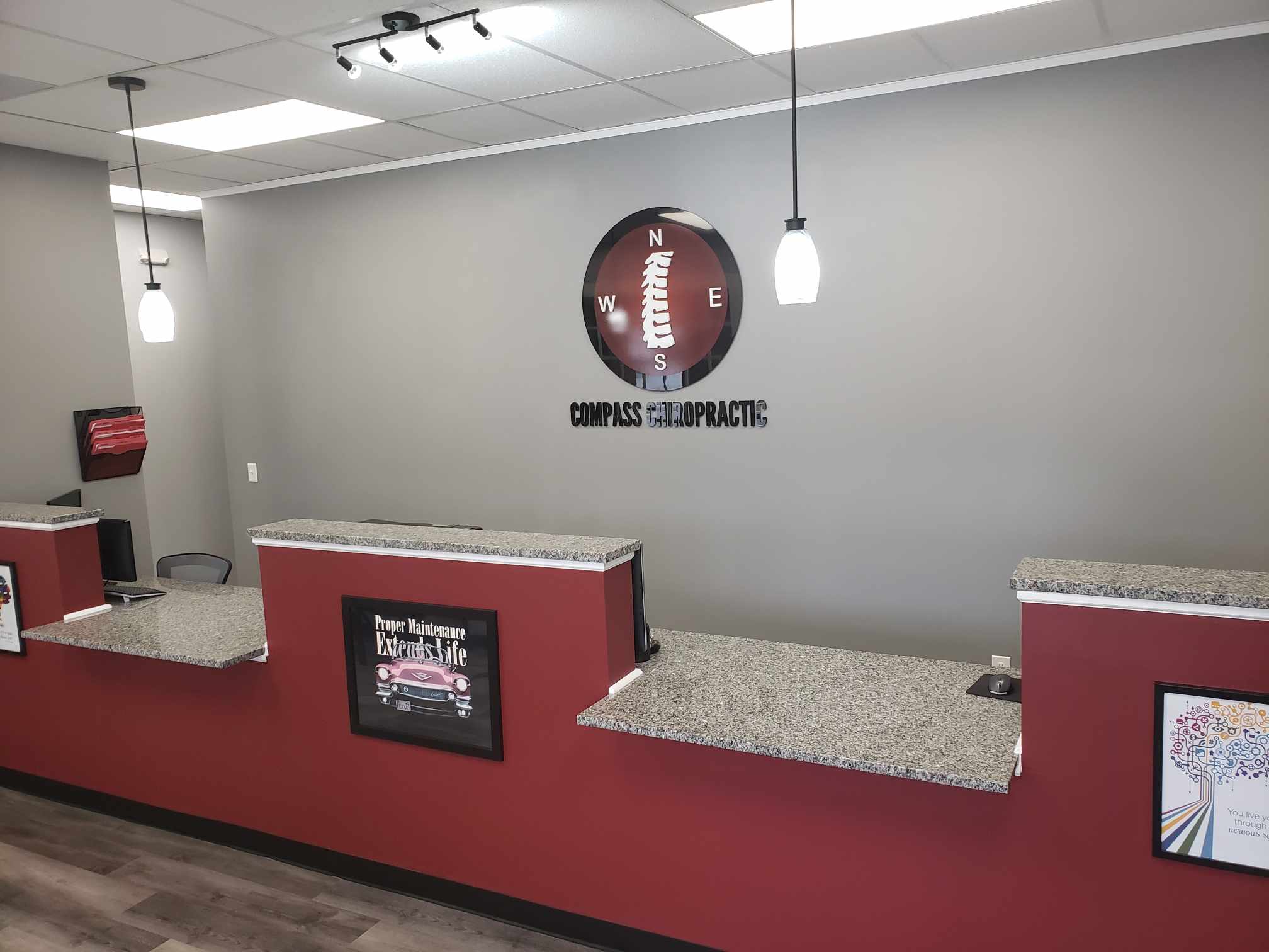 Compass Chiropractic front desk: red counter with granite top and the compass logo on a gray wall